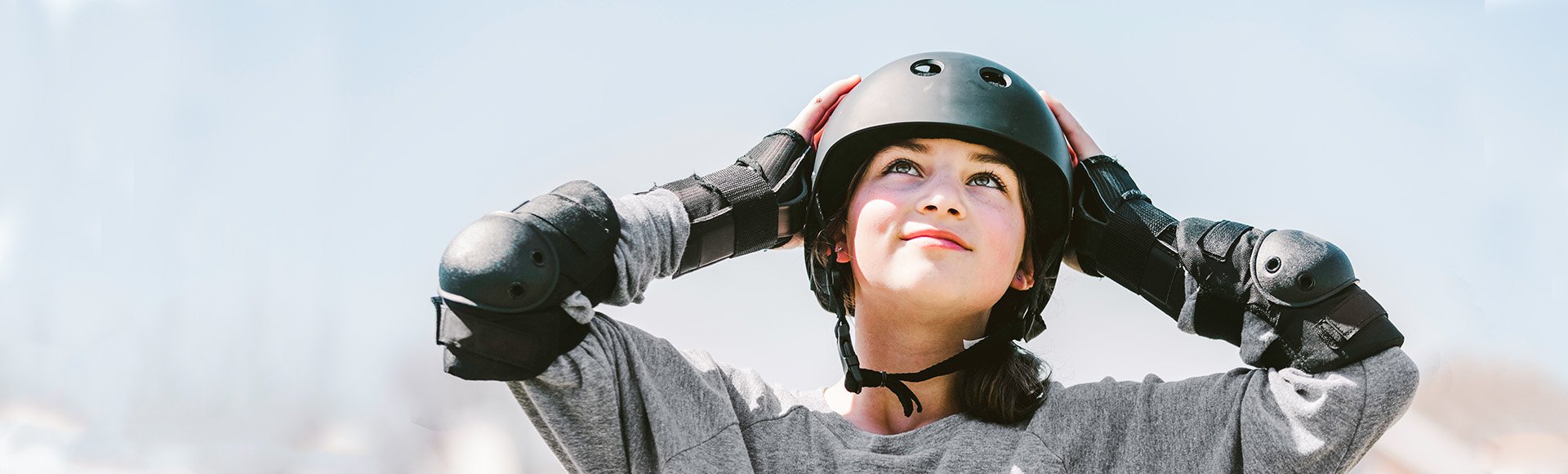 teenage girl wearing helmet and other skateboard protective gear, looks up at sky